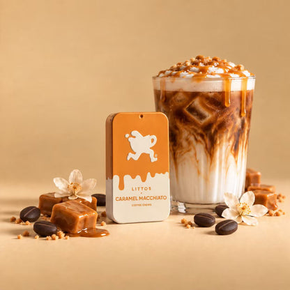 A glass of caramel macchiato iced coffee with caramel drizzle and whipped cream, styled with caramel cubes, coffee beans, and white flowers beside a branded product box labeled &